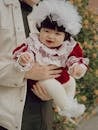 Cute baby dressed in festive red and lace held by an adult, with a warm smile.